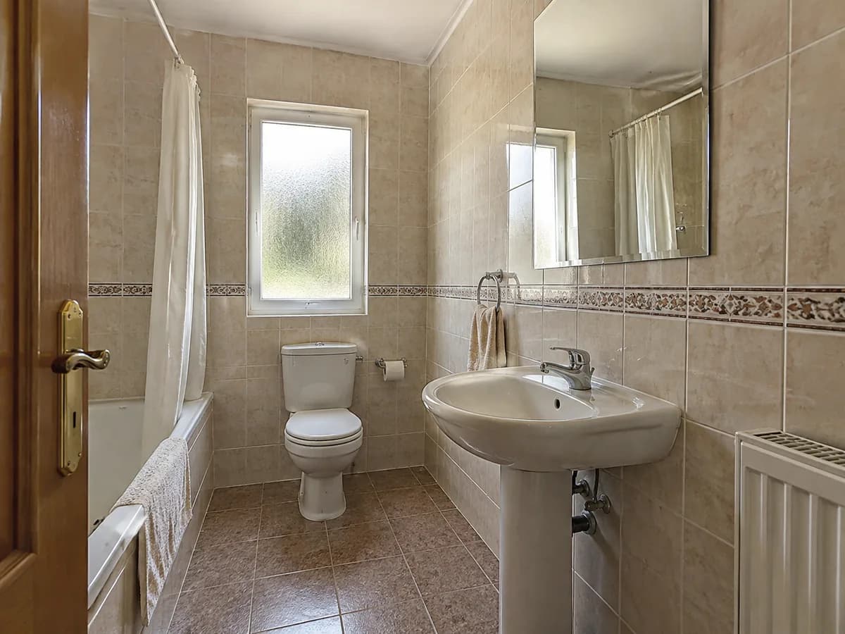 A dated bathroom with glossy beige wall tiles, a decorative border, brown floor tiles, a bathtub and a pedestal sink