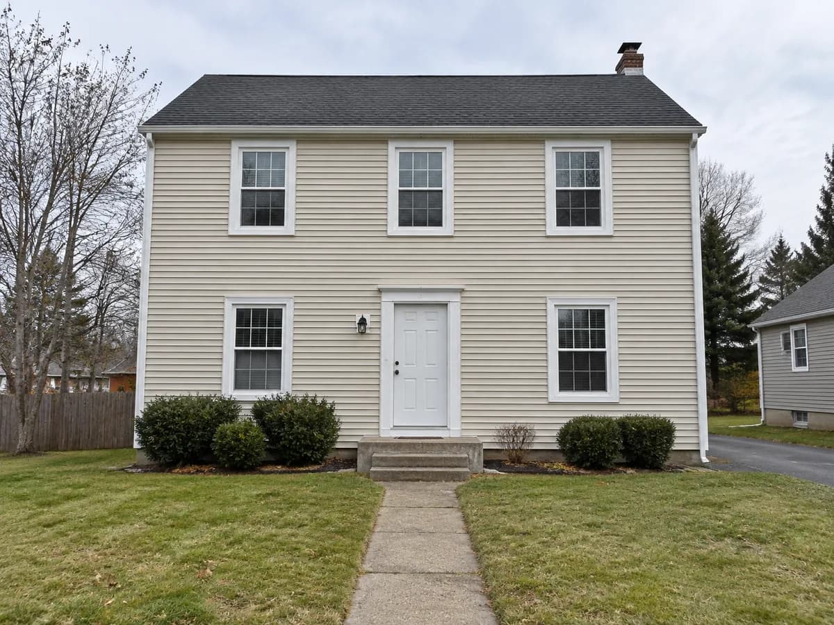 A two-story colonial house with beige siding and a white front door before the change