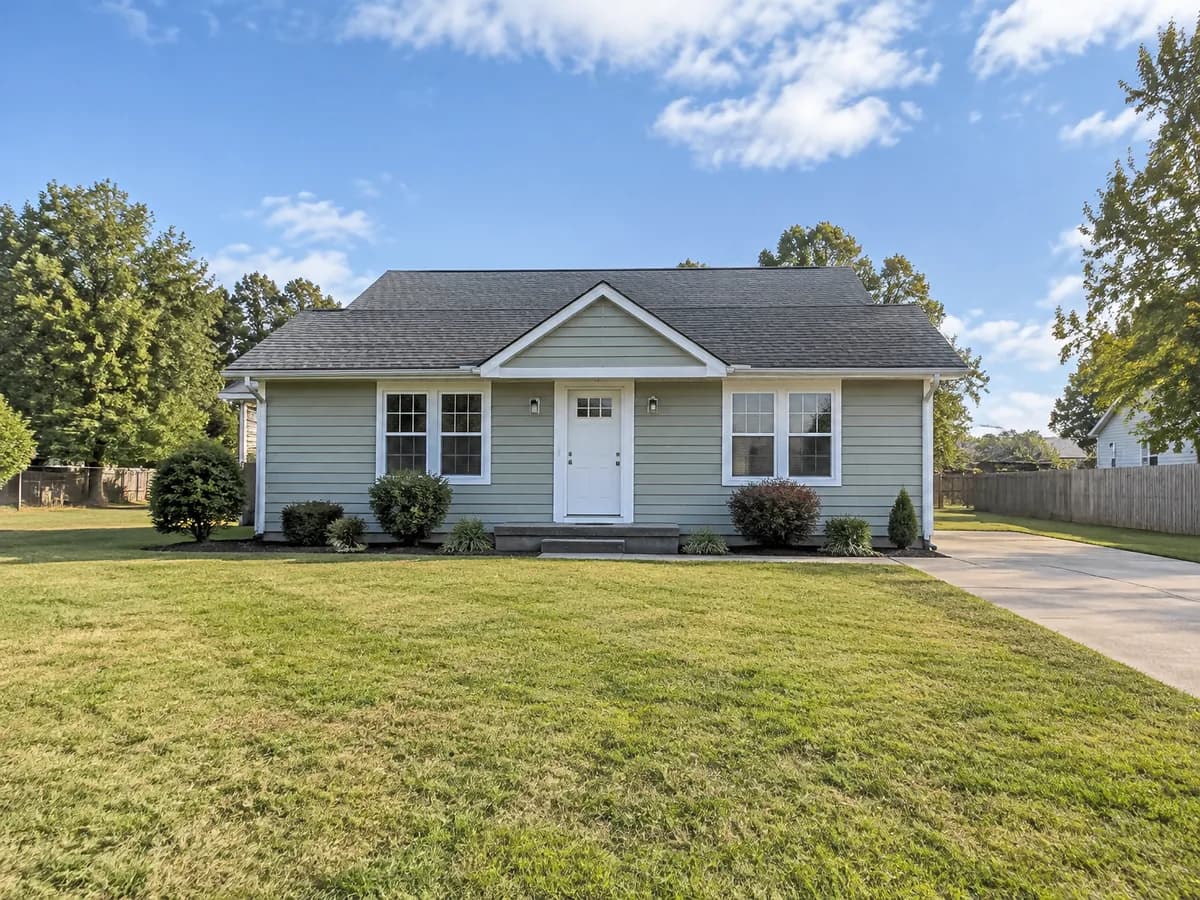 A one-story sage green bungalow on a wide lawn before the addition